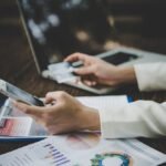 Osoba koristi mobilni telefon za upravljanje finansijama uz laptop i izveštaje