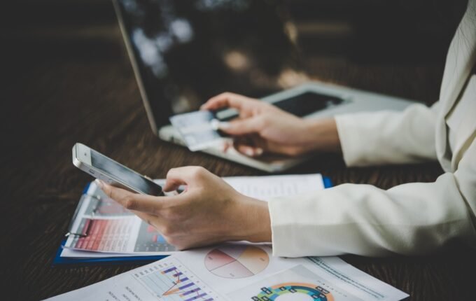Osoba koristi mobilni telefon za upravljanje finansijama uz laptop i izveštaje
