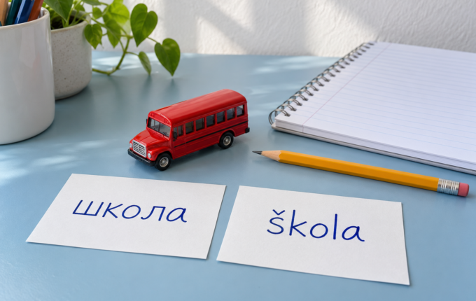 Kartice sa ćiriličnim zapisom школа i latiničnim škola uz svesku, olovku i crveni autobus igračku.